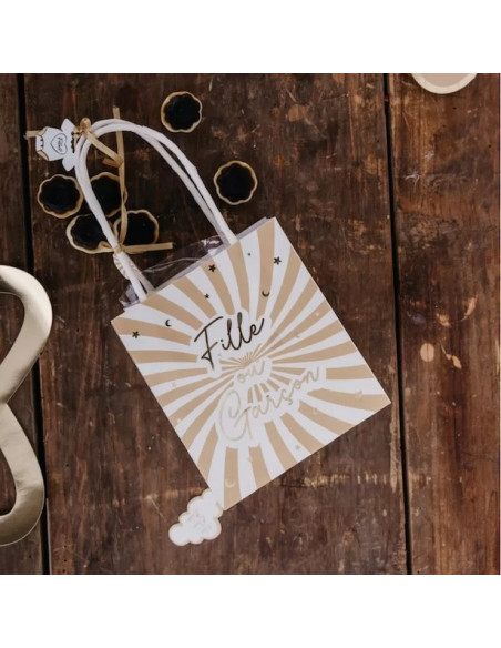 Sacs cadeaux « Fille ou Garçon » – Révélation du sexe du bébé, boîte cadeau beige à rayons crème sur plancher en bois.