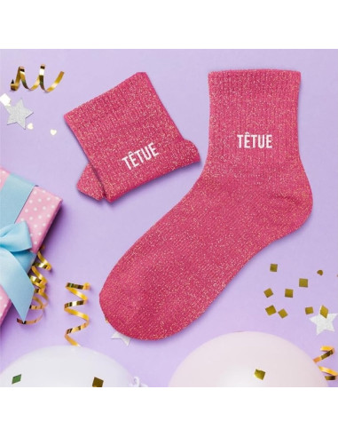 Pinke Glitzersocken für Damen „STUBBORN“ mit TETUE-Logo auf lilafarbigem Hintergrund, daneben passende Stulpen; festliche Dekora