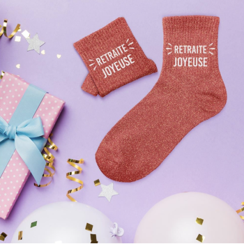 Pinke Glitzersocken mit Aufschrift „RETRAITE JOYEUSE“ und passende Glitzer-Butteroschetten neben Geschenk verziert mit Pfeifen.