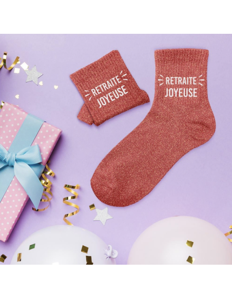 Pinke Glitzersocken mit Aufschrift „RETRAITE JOYEUSE“ und passende Glitzer-Butteroschetten neben Geschenk verziert mit Pfeifen.