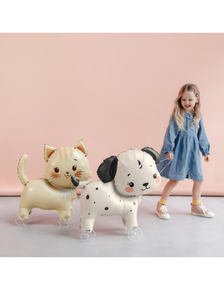 Katzenballon auf Rädern: kleines Mädchen in blauem Kleid zieht zwei ballonierte Katzen mit Rädern, hellbeige und weiß mit schwar