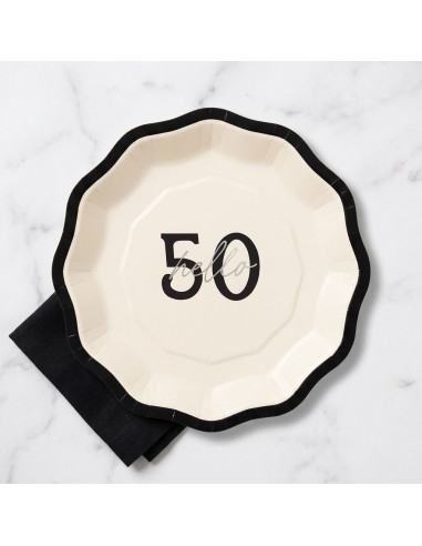 Assiette Hello 50 en crème avec bord noir ondulé, motif “50” au centre, posé sur nappe marbrée.