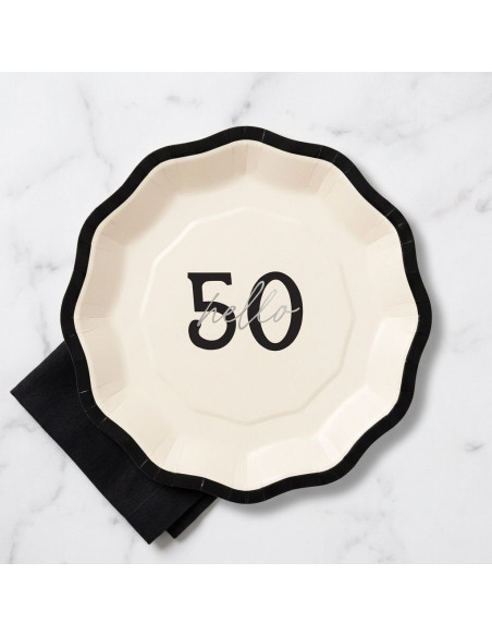 Assiette Hello 50 en crème avec bord noir ondulé, motif “50” au centre, posé sur nappe marbrée.